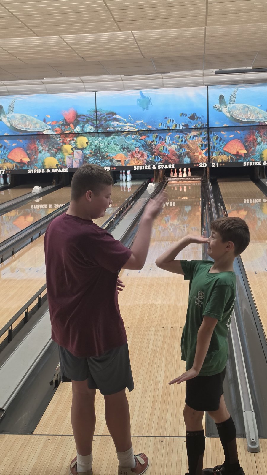 Two young people raise their hands toward one another for a high-five beside the bowling lanes.